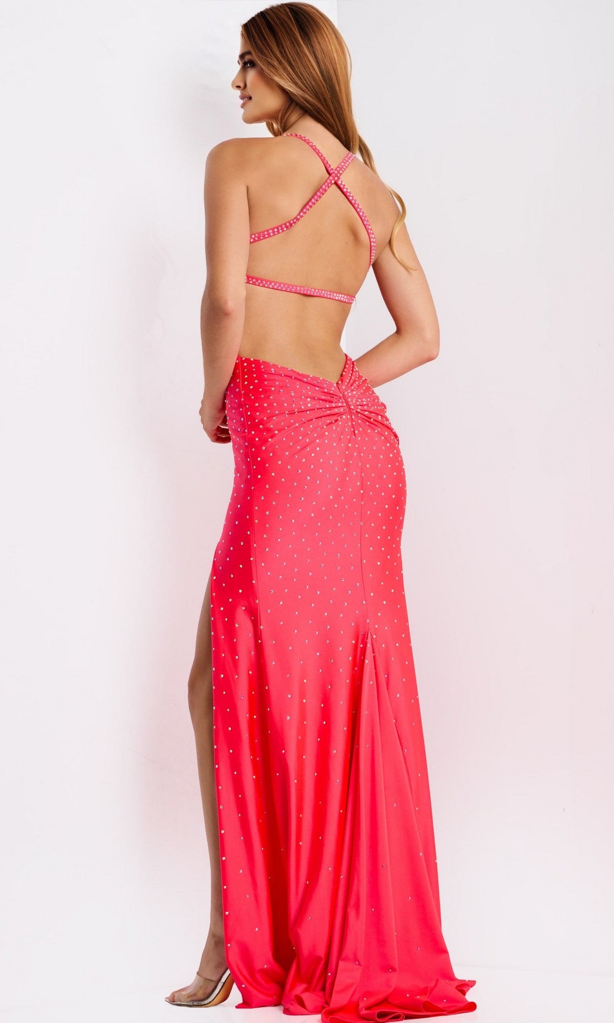 A woman models the Jovani 48070 long prom dress, featuring a floor-length sheath silhouette, pink color, thin crisscross straps, and rhinestone embellishments against a plain white background.